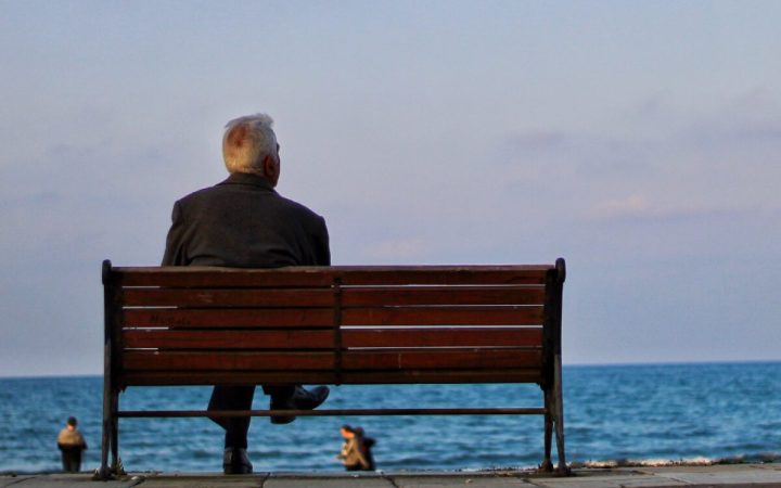 bărbat cu părul alb care privește în zare pe malul mării
