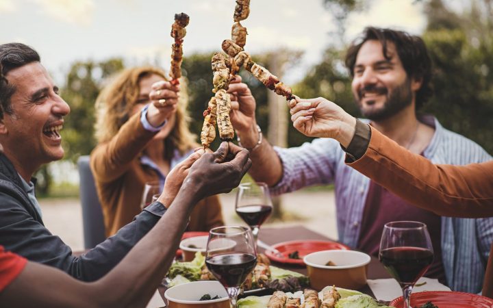 Prieteni care ciocnesc frigărui cu carne la prânz