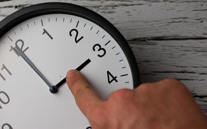 bărbat care schimbă cu degetul ora ceasului de la 4.00 la 3.00 pentru a trece la ora de iarnă 2025