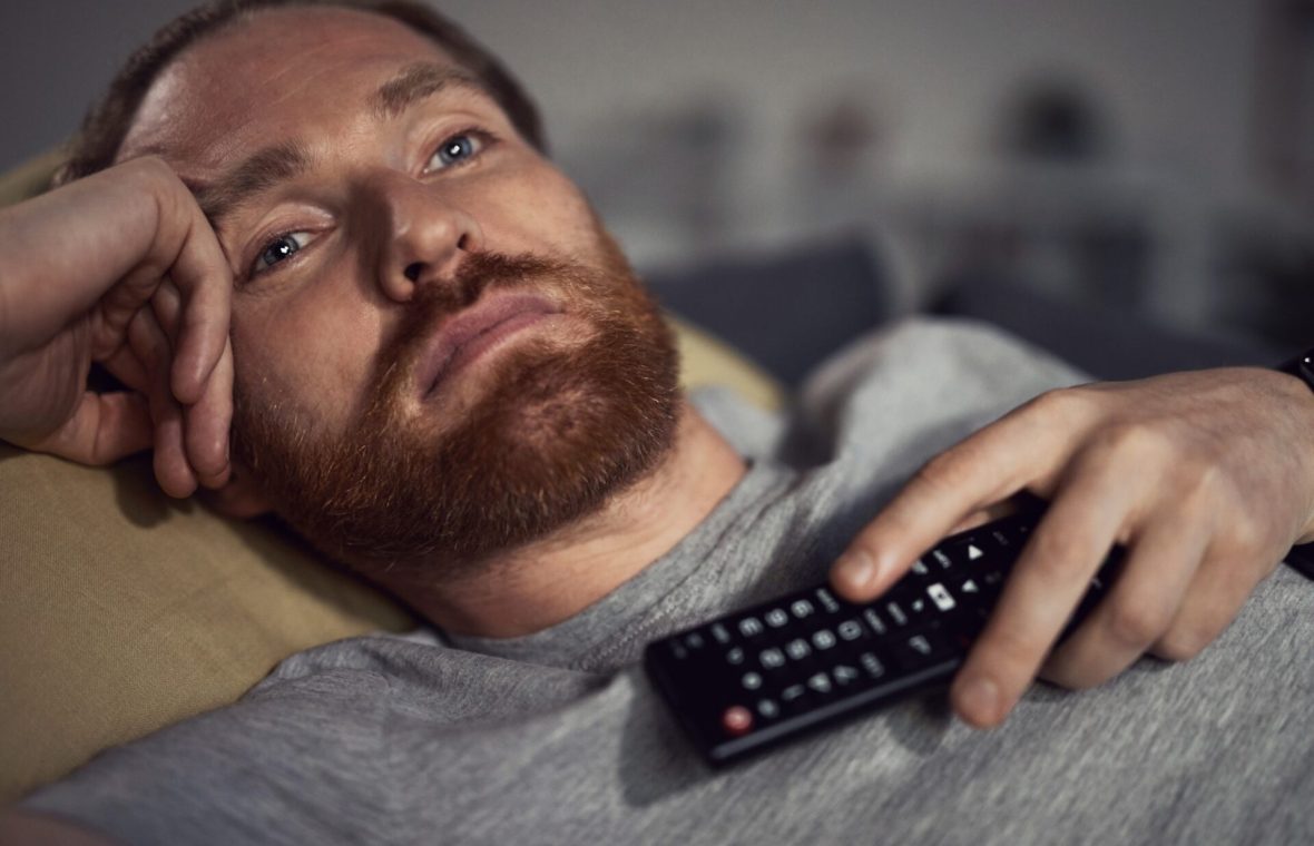 bărbat privește în gol la televizor cu telecomanda pe piept
