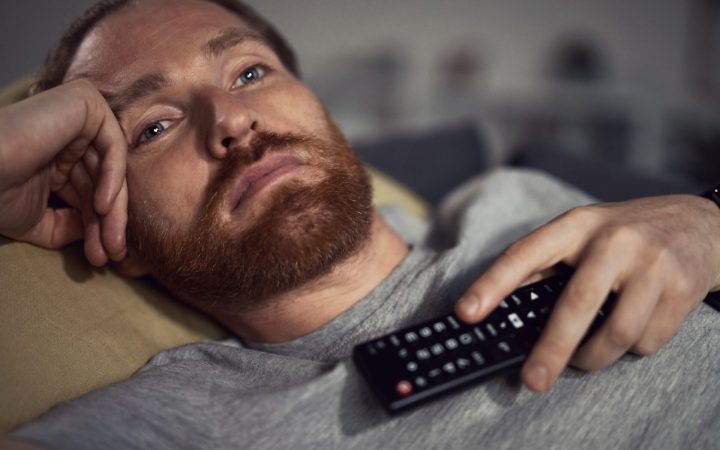 bărbat privește în gol la televizor cu telecomanda pe piept