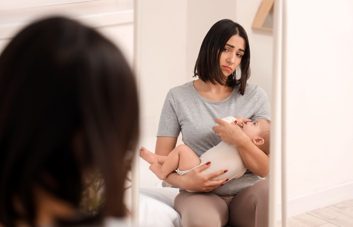 mamă în oglindă cu bebelușul în brațe tristă pentru că soțul este interesat de altă femeie