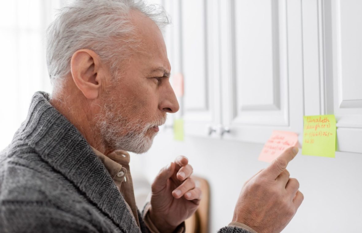 bărbat în vârstă, cu boala Alzheimer, verifică notițele de pe post-it-uri pe mobilă