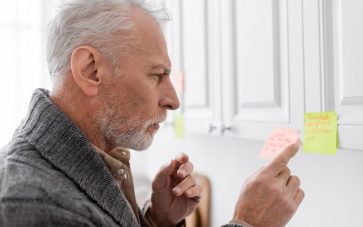 bărbat în vârstă, cu boala Alzheimer, verifică notițele de pe post-it-uri pe mobilă