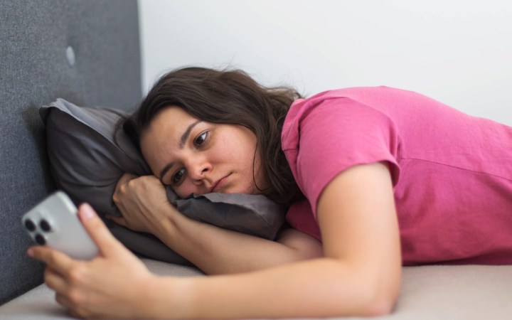 femeie care stă în pat și se uită pe telefon