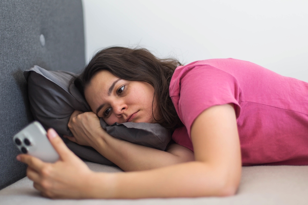femeie care stă în pat și se uită pe telefon