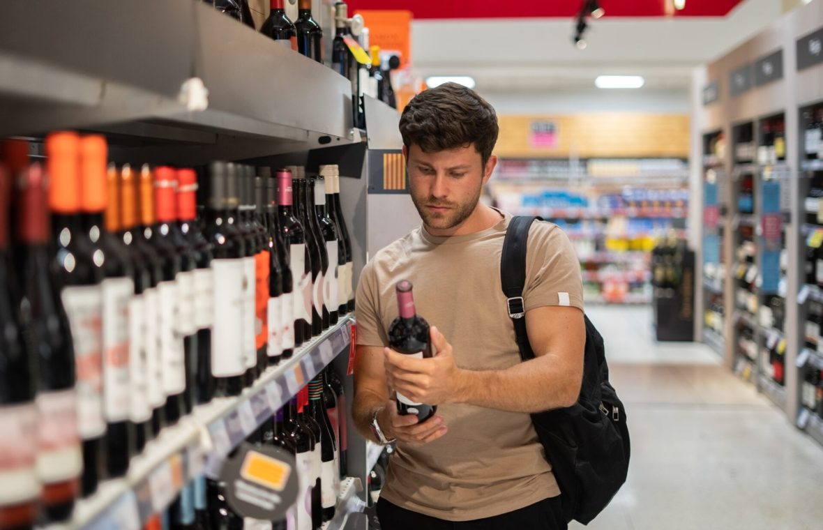 bărbat la magazin, care alege ce tip de alcool să cumpere