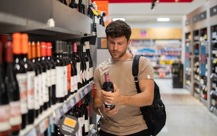 bărbat la magazin, care alege ce tip de alcool să cumpere