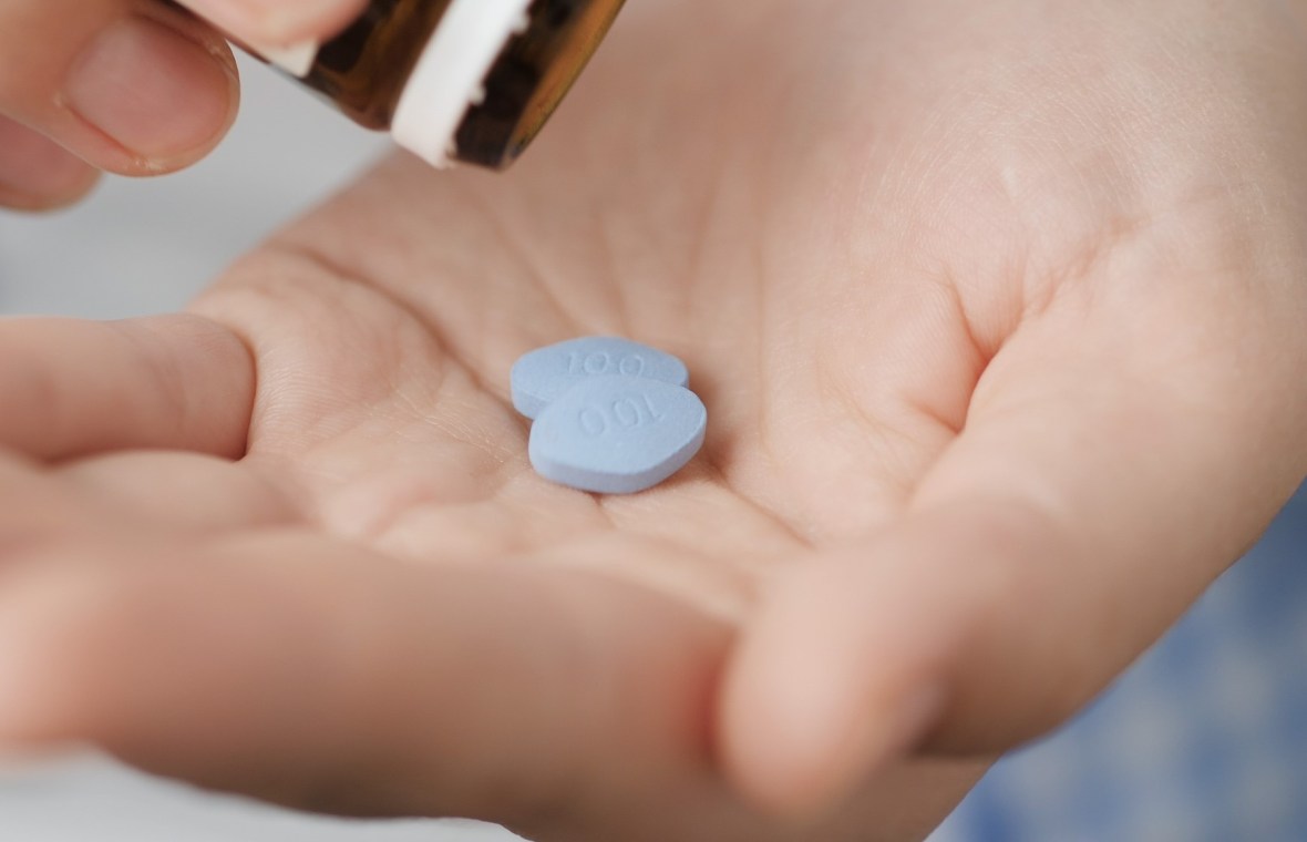 bărbat își pune în palmă două pastile albastre de viagra pentru potență