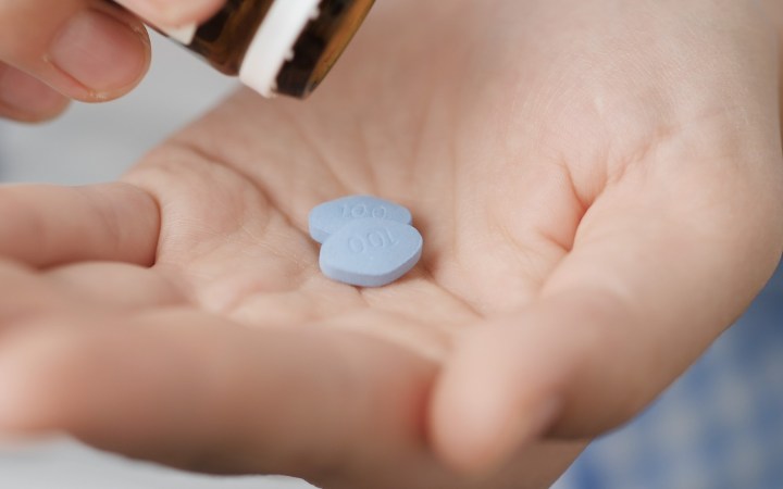 bărbat își pune în palmă două pastile albastre de viagra pentru potență